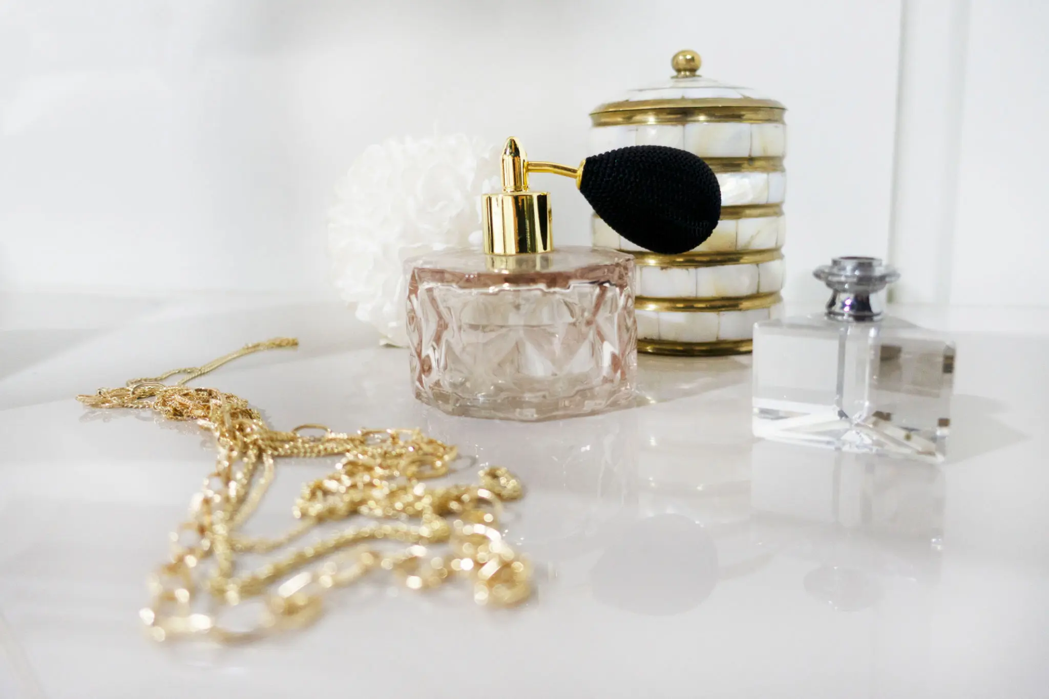 Elegant vanity items including perfume bottles and gold chain on a white surface.