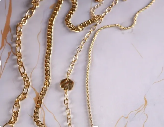 Close-up of gold chains and a gemstone bead on a white marble surface.